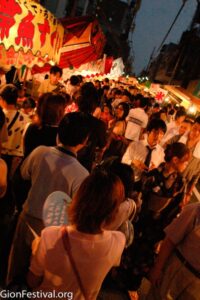 Crowds walk down a street lined with food and game stalls  at the Gion Festival.