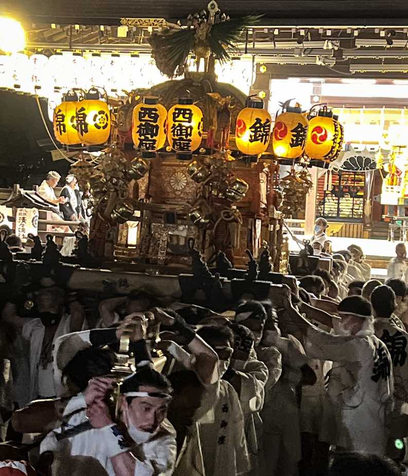 Scores of men carry a golden, decorated portable shrine on their shoulders at Yasaka Shrine during Kyoto's GIon Festival. 