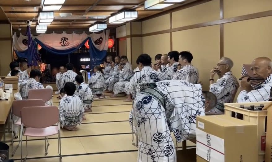 Men in yukata practice the Gion Festival music at kanko Boko, while one records his temperature as a covid safety precaution, Gion Festival.