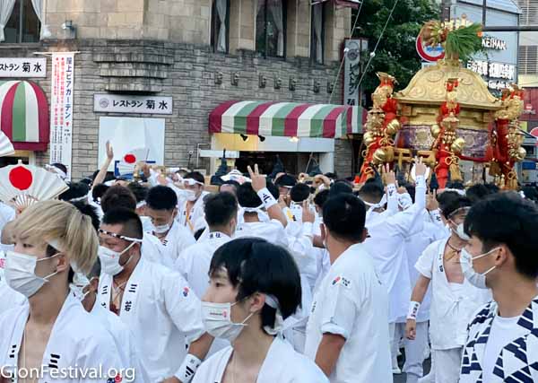 Many men wearing white traditional costume carry a golden portable mikoshi shrine during the shinkosai on the evening of July 17.