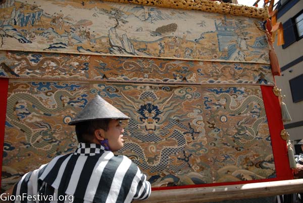 Vintage textiles decorate the side of Ennogyoja Yama, including one of a blue dragon, while a man in traditional Japanese costume moves the float in the July 24 procession.