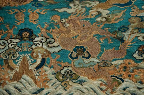 Antique Chinese textile depicting a blue dragon flying above sea waves and rocks. 