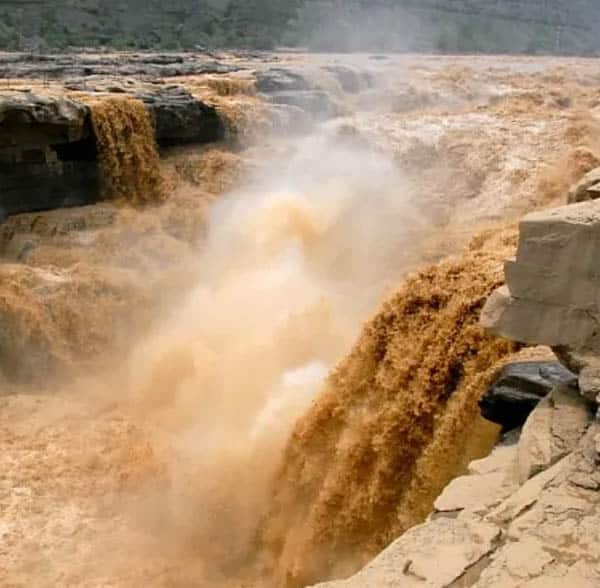 Torrents of brown water crash down river rapids.